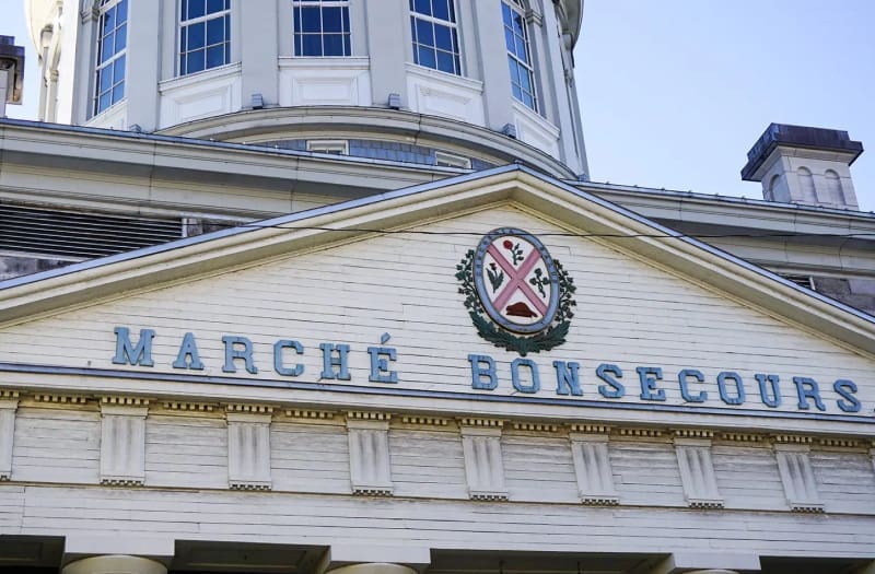 La photo montre la façade du Marché Bonsecours à Montréal, sur laquelle figurent un blason et le nom du bâtiment en lettres bleues sous un dôme.